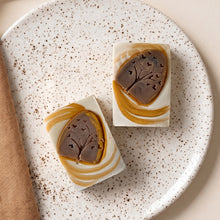 Load image into Gallery viewer, Two fall handmade soap bars with cream bases, ochre swirls, and raised brown tree-and-heart designs.