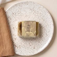 Load image into Gallery viewer, Wrapped artisan soap bar with visible cream-and-ochre handmade soap and Woods &amp; Mosses paper sleeve.