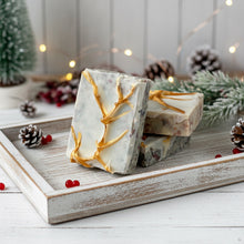 Load image into Gallery viewer, Three rectangular artisan soaps with a frosted white base and embedded natural speckles, decorated with golden branch-like accents on the surface, creating an elegant festive design.
