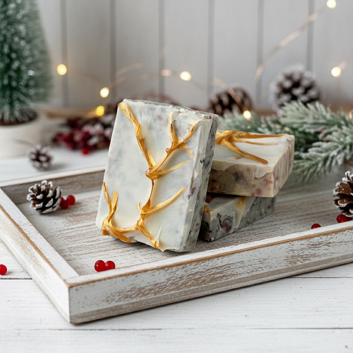 Three rectangular artisan soaps with a frosted white base and embedded natural speckles, decorated with golden branch-like accents on the surface, creating an elegant festive design.