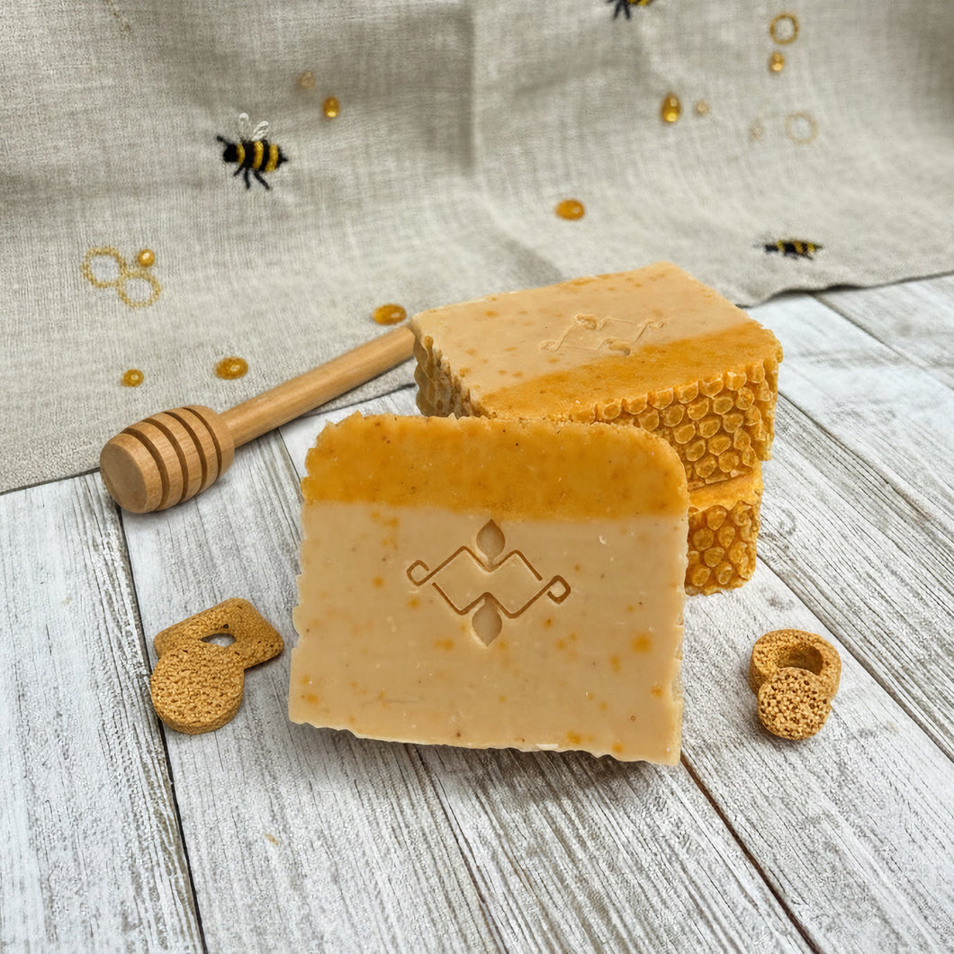 Square soap bar, two-toned yellow with a Woods and Mosses logo. Features tiny honey dots and a textured honeycomb design on top.