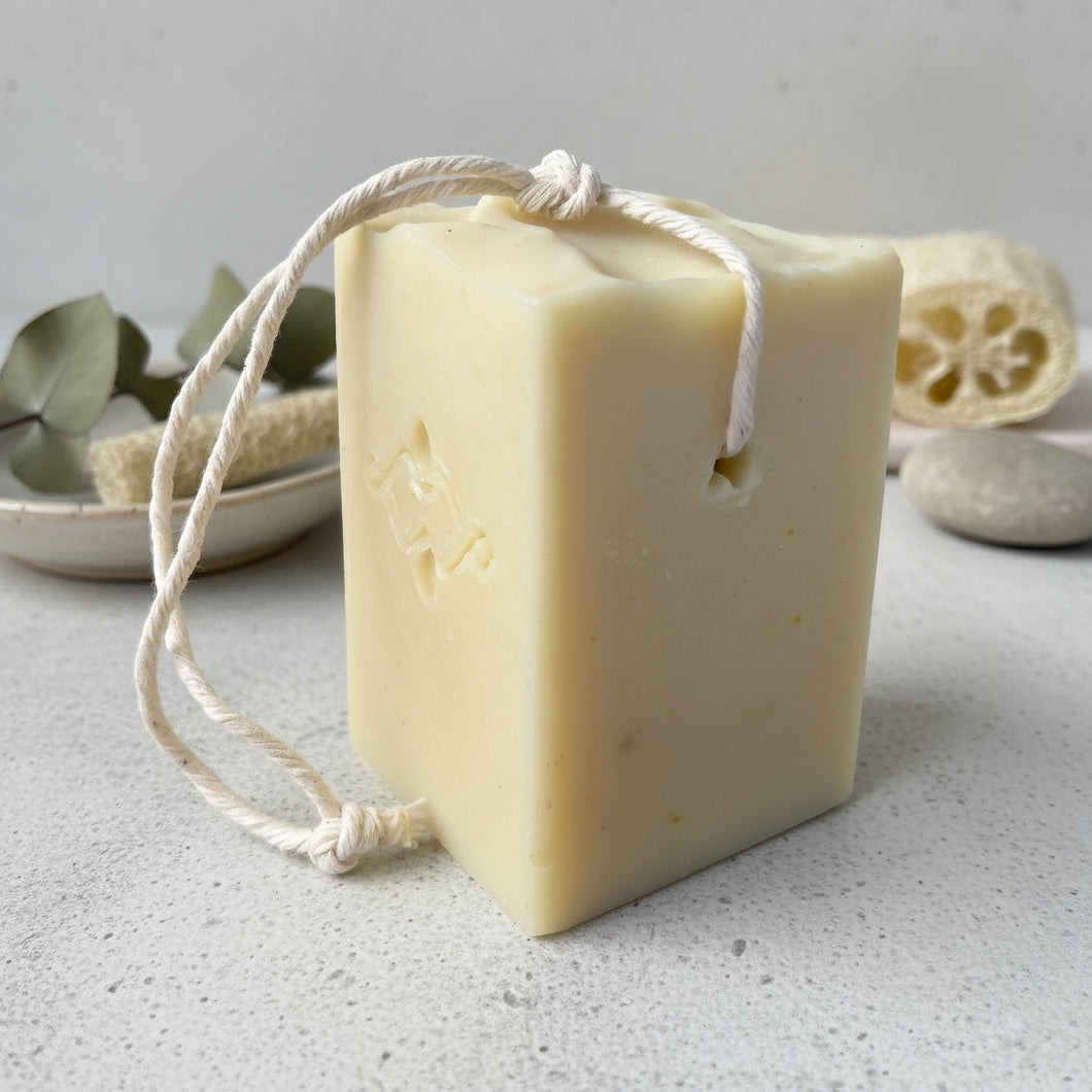 Natural rectangular tallow soap bar with cotton rope, embossed with Woods and Mosses artisan logo, solid creamy beige color, designed for dish and laundry cleaning.