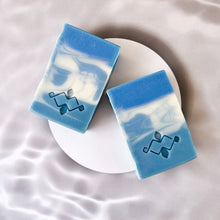 Load image into Gallery viewer, A square soap bar with vivid blue and white swirls features a stamped Woods and Mosses logo on its smooth surface. The design evokes a sense of Arctic freshness, with striking contrasts between the rich blue and crisp white colors.