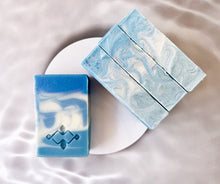 Load image into Gallery viewer, A square soap bar with vivid blue and white swirls features a stamped Woods and Mosses logo on its smooth surface. The design evokes a sense of Arctic freshness, with striking contrasts between the rich blue and crisp white colors.