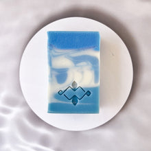 Load image into Gallery viewer, A square soap bar with vivid blue and white swirls features a stamped Woods and Mosses logo on its smooth surface. The design evokes a sense of Arctic freshness, with striking contrasts between the rich blue and crisp white colors.