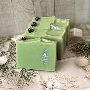 A pale green square soap with a handpainted silver Christmas tree. The bar has a wavy top decorated with a pinecone.