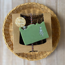 Load image into Gallery viewer, A pale green square soap with a handpainted silver Christmas tree. The bar has a wavy top decorated with a pinecone.