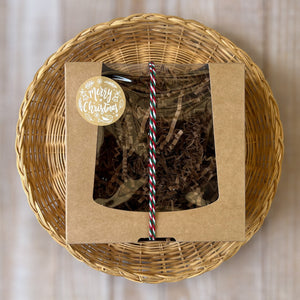 A kraft box with a transparent lid filled with brownish soap, tied with a festive white, red, and green rope and adorned with a Merry Christmas sticker.