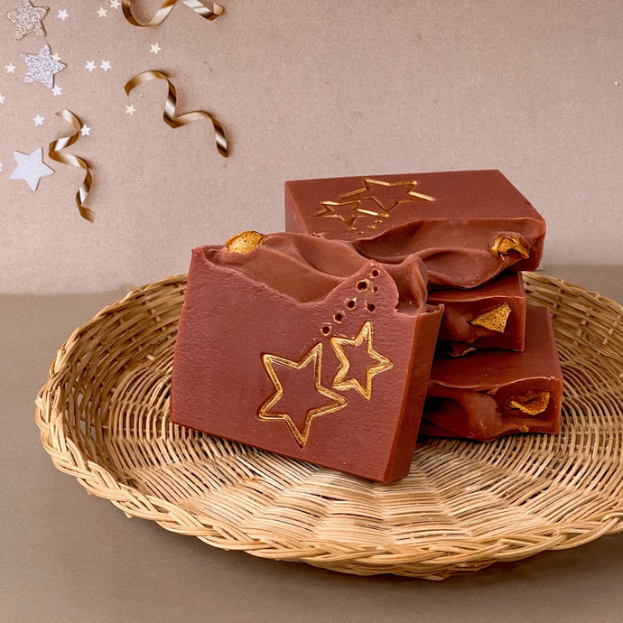 A red-brownish square soap with handpainted golden stars. The bar has a wavy top decorated with an orange slice.