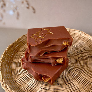 A red-brownish square soap with handpainted golden stars. The bar has a wavy top decorated with an orange slice.