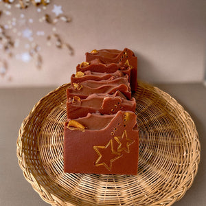 A red-brownish square soap with handpainted golden stars. The bar has a wavy top decorated with an orange slice.