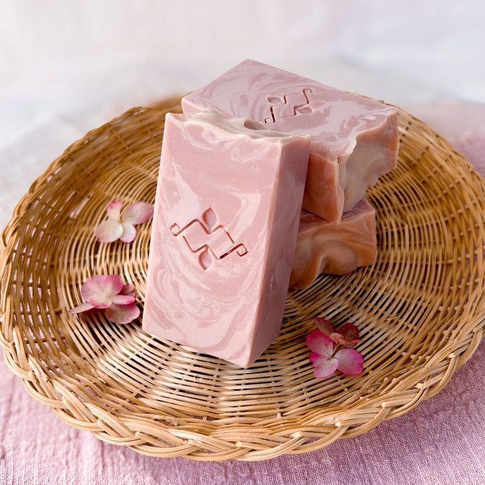 Powdery rose-colored tall soap bar with pale-rose swirls and a wavy textured top. It features a Woods and Mosses company stamp on its surface.