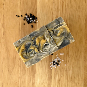 A soap with distinct white, black, and yellow layers, featuring a textured top. 