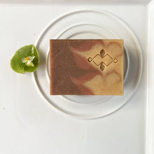 Load image into Gallery viewer, Handmade soap bar with beige, dusty rose, and brown swirls. The Woods and Mosses company logo is prominently displayed in the lower corner.