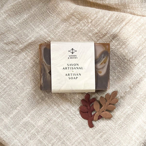 A single bar of marbled caramel and chocolate soap is wrapped in minimalist packaging that reads Woods & Mosses and Savon Artisanal - Artisan Soap.