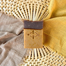 Load image into Gallery viewer, A handcrafted soap bar with two distinct layers: a light beige base and a brown top, divided by a visible seam. The soap has a decorative stamp on the front.