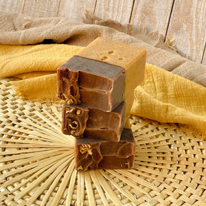 A stack of three handcrafted soap bars with a light beige bottom and a rich brown top. The bars have textured tops adorned with orange peel. 