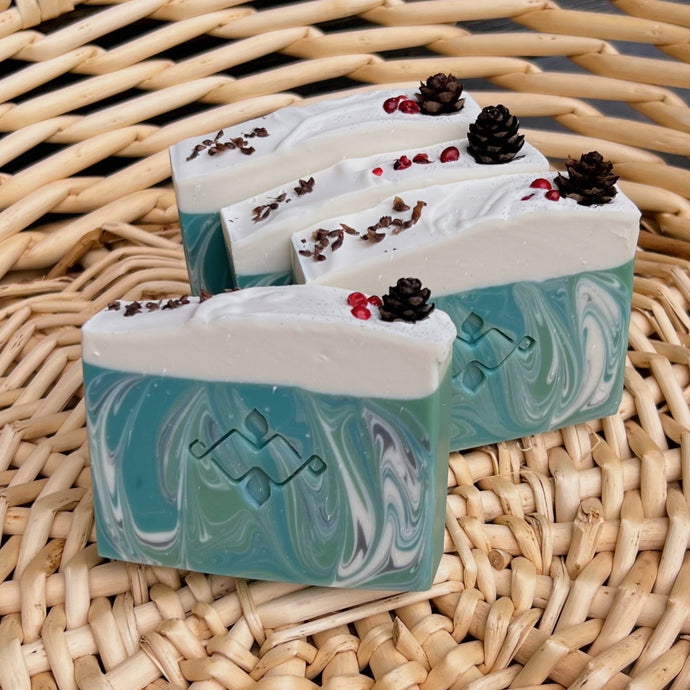 Textured, square soap bar swirled with green, white, and blue hues. Features a central Woods and Mosses company logo and a glitter-dusted pine cone on top.