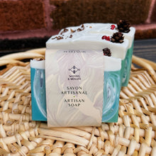 Load image into Gallery viewer, The soap bar is labeled and wrapped with recyclable paper for an eco-friendly touch. The label features the Woods and Mosses company logo and the words Artisan Soap in both French and English.