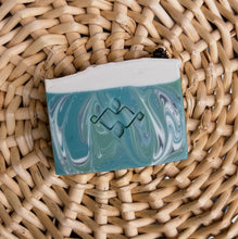 Load image into Gallery viewer, Textured, square soap bar swirled with green, white, and blue hues. Features a central Woods and Mosses company logo and a glitter-dusted pine cone on top.