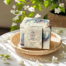 Load image into Gallery viewer, Artisan soap bar with Woods and Mosses packaging on a woven tray surrounded by flowers
