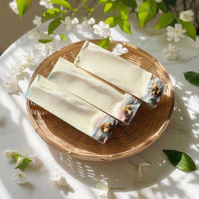 Load image into Gallery viewer, Bar of soap with floral elements on a woven plate surrounded by flowers and leaves