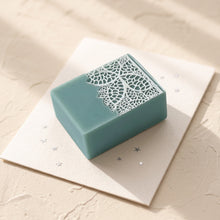Load image into Gallery viewer, Greenish-blue Christmas lace soap bar with intricate white botanical lace detail, shown at an angle.