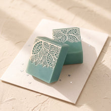 Load image into Gallery viewer, Two greenish-blue handmade soap bars with different white lace patterns, displayed upright and leaning.