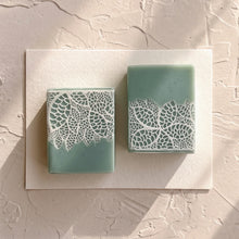 Load image into Gallery viewer, Two greenish-blue artisan soap bars in a flat lay, showing contrasting white lace designs.