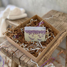 Load image into Gallery viewer, Square soap bar, white with purple swirls, featuring a company logo. The soap top is white-purple and decorated with a pinch of glitter.