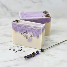 Load image into Gallery viewer, Handmade lavender soap bars featuring a smooth ivory base and a vibrant purple marbled top. One bar reveals Woods and Mosses logo, both are garnished with dried lavender buds for a natural touch.