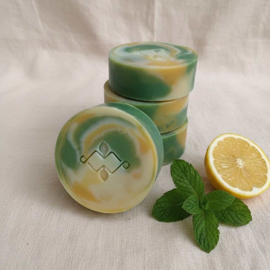 Round lemon and peppermint artisan soap bar with green and yellow swirls and Woods and Mosses logo.