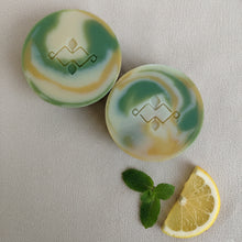 Load image into Gallery viewer, Two vegan artisan soaps with green and gold swirl pattern and embossed design.
