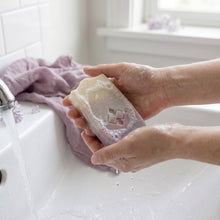 Load image into Gallery viewer, Single lilac soap bar with stamped logo, wet surface and light foam on pastel layers