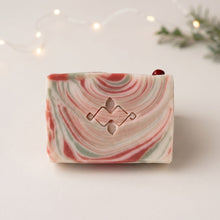 Charger l'image dans la galerie, Front view of a cream Christmas soap bar with red and pale green swirls, red jasper stone, and stamped geometric Woods and Mosses logo