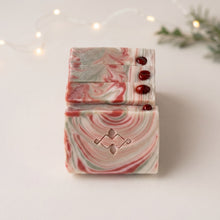 Charger l'image dans la galerie, Stack of red, cream, and pale green Christmas soap bars with red jasper stones and a stamped geometric logo.