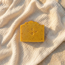 Load image into Gallery viewer, Single handmade mango soap bar with logo stamp and warm yellow color, shown from above.