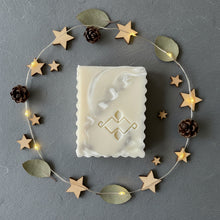 Load image into Gallery viewer, natural shea butter marble soap bar shown flat with a carved logo surrounded by wooden stars and small pinecones