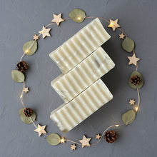 Load image into Gallery viewer, three natural marble soap bars with textured edges surrounded by a minimalist circle of wooden stars and pinecones
