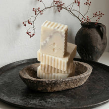 Load image into Gallery viewer, Three bars of soap stacked in a rustic stone bowl with a vase and branches in the background.
