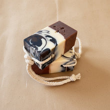 Load image into Gallery viewer, Tall soap bar on beige rope, with a brown base, white center featuring brown and black swirls, and Woods and Mosses logo on the brown bottom.