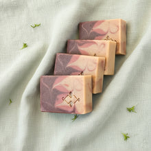 Load image into Gallery viewer, Artisan soap bars with beige, dusty rose, and brown swirls. The company logo is prominently displayed in the lower corner.