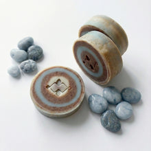 Load image into Gallery viewer, Three round swirl soap bars arranged vertically, highlighting their blue and brown layered pattern and carved center.