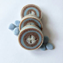 Load image into Gallery viewer, Three round swirl soap bars arranged flat, showing blue and brown layered rings and a centered carved pattern