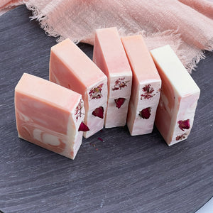 Lineup of five natural rose soap bars, each with soft marbled colors and dried rosebuds, showcasing the floral topping and minimalist cut edges.