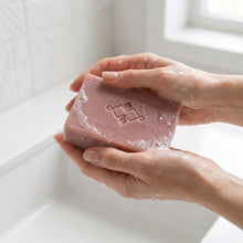 Load image into Gallery viewer, Rosehip artisan soap bar in use, wet and lightly lathered, with the embossed logo visible on the smooth surface.