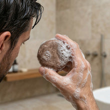 Load image into Gallery viewer, Man holding a shampoo bar with foam in a bathroom setting