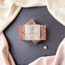 Charger l'image dans la galerie, Two pink silk soap bars crossed with a bilingual artisan soap label, rose base, and floral swirl design