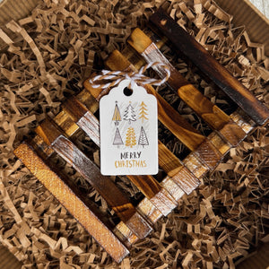 Wooden soap tray placed in kraft paper shred, decorated with a holiday gift tag that reads Merry Christmas and features small Christmas trees in green, brown, and gold tones.