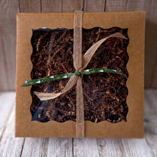 Load image into Gallery viewer, A brown kraft gift box with a clear window is filled with raffia paper and tied with brown and green ribbons.